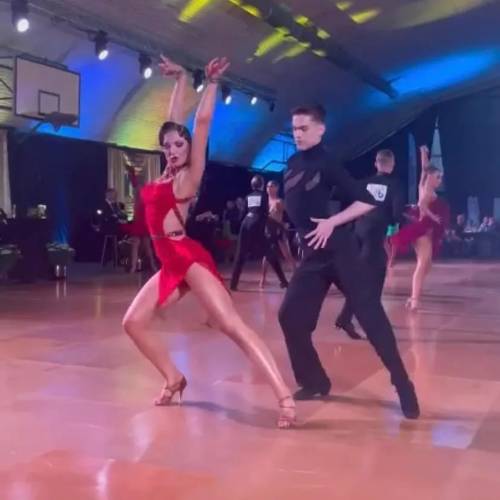 Zawodnicy podczas prezentacji tańca. Kobieta w czerwonej  obcisłej sukience i jej partner taneczny w czarnym komplecie.